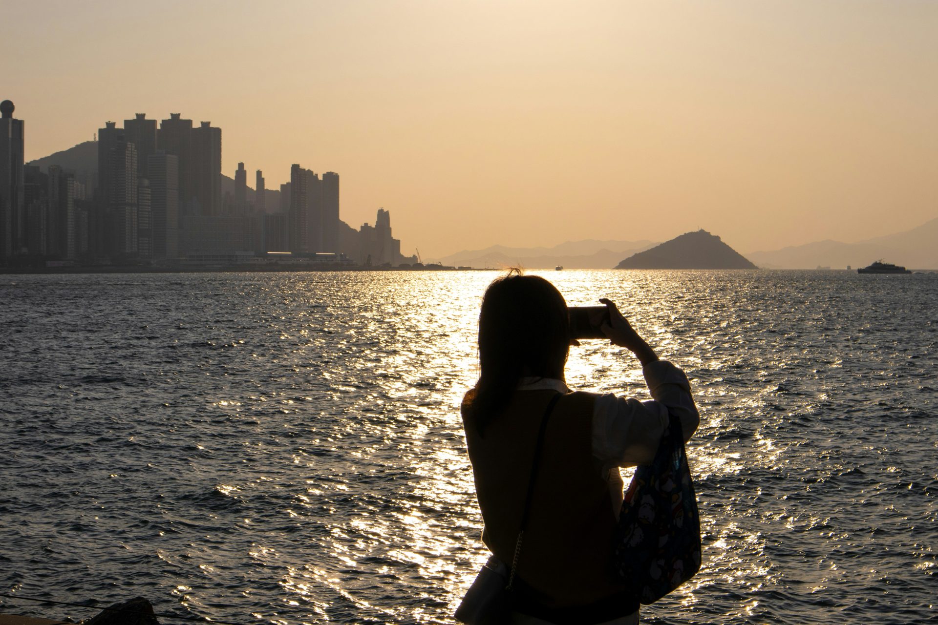 a woman taking a picture of the sun setting over the water